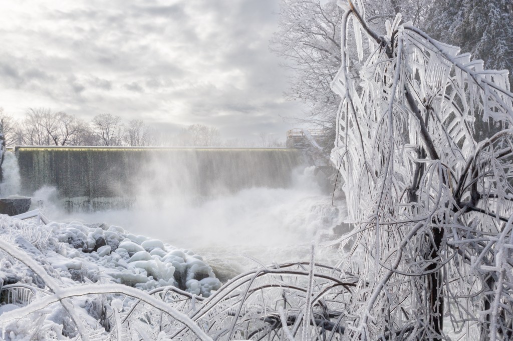 Cloudy skies, ice and snow covered branches, spray from the waterfall